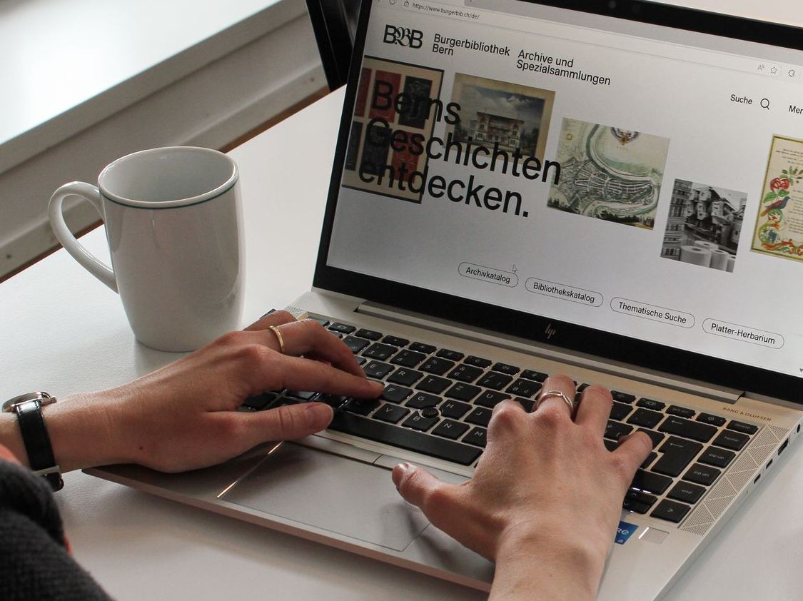 Eine Person, welche die Webseite der Burgerbibliothek Bern an einem Laptop besucht.