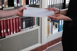 Eine Person nimmt eine Mappe vom Lesesaalpersonal entgegen.