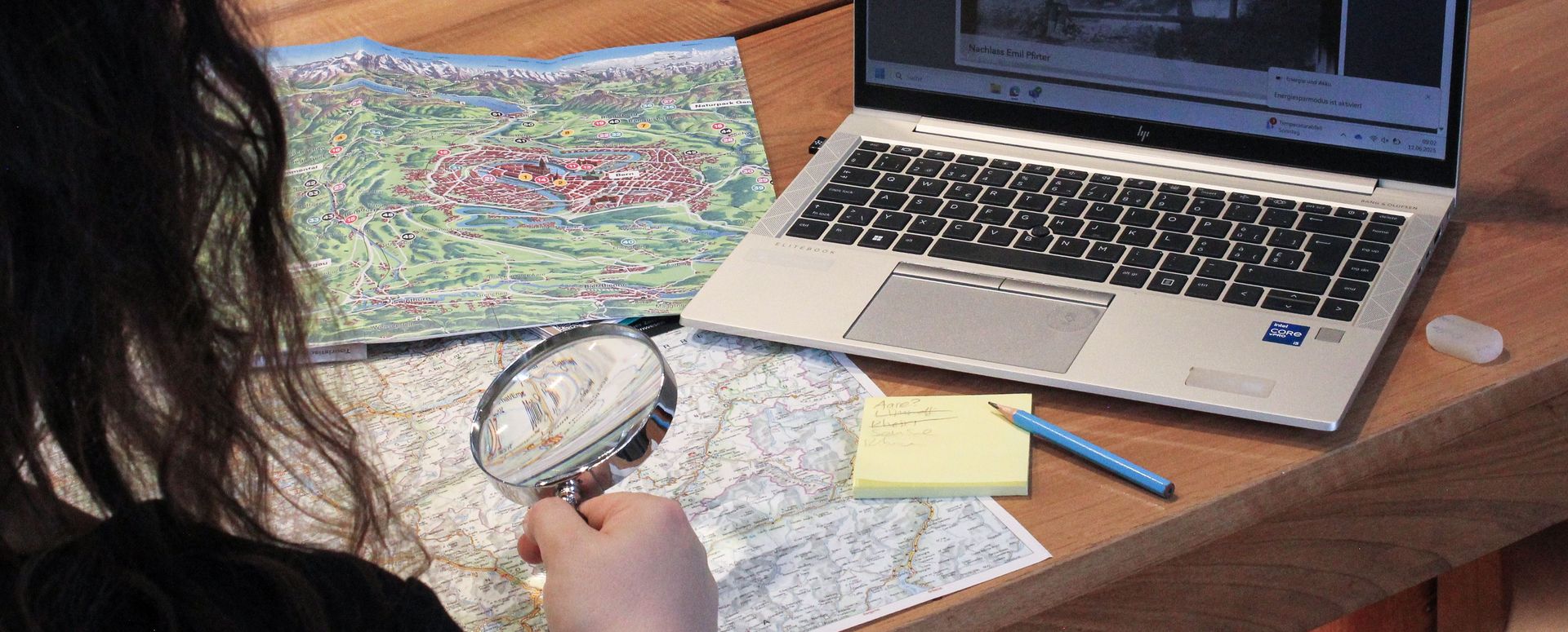 Eine Person untersucht Archivalien mit einer Lupe und macht sich Notizen dazu.